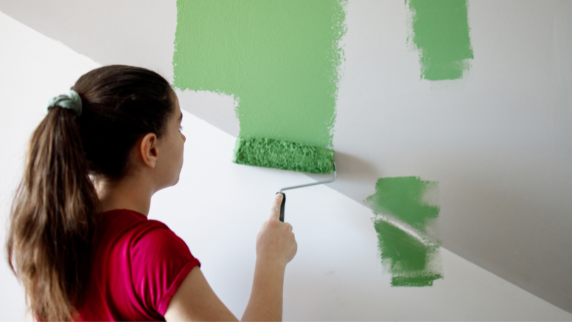 woman using green paint roller on white wall